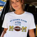 Woman wearing a personalized Football Mom shirt with custom player name, embroidered MOM lettering, and real leather football applique.