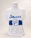 White personalized Soccer Mom performance shirt with blue appliqué letters, a leather soccer ball, embroidered name ARRIA, and red heart accents on a mannequin.