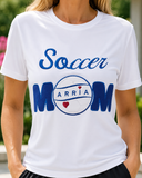 Personalized white Soccer Mom performance shirt with blue embroidery, twill appliqué, a white leather soccer ball, the name ARRIA, and red heart accents.