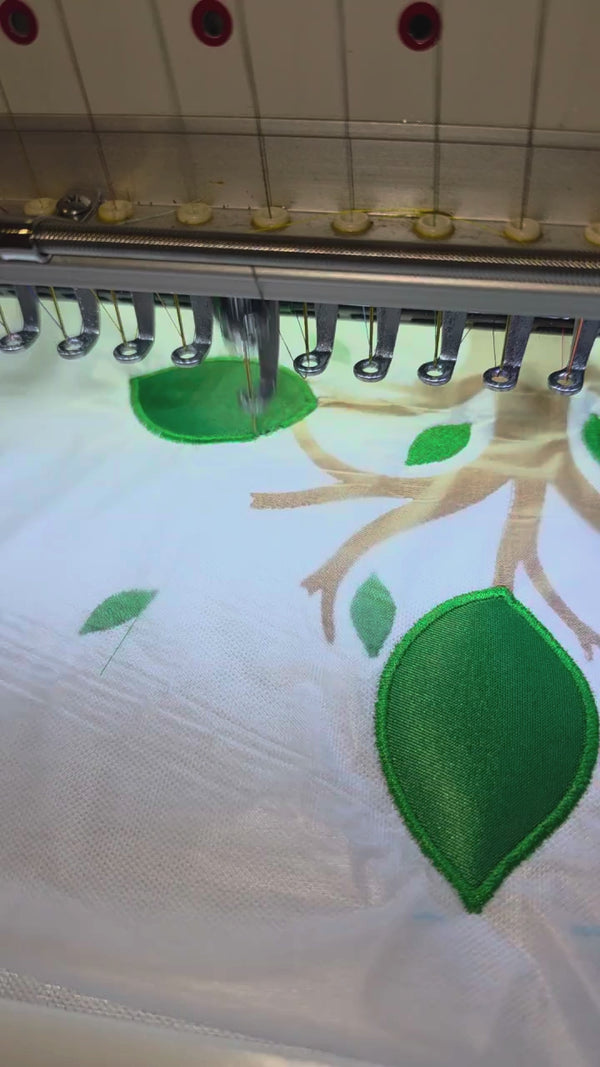 Commercial embroidery machine creating personalized tackle-twill leaves and an embroidered family tree design for a custom family reunion polo