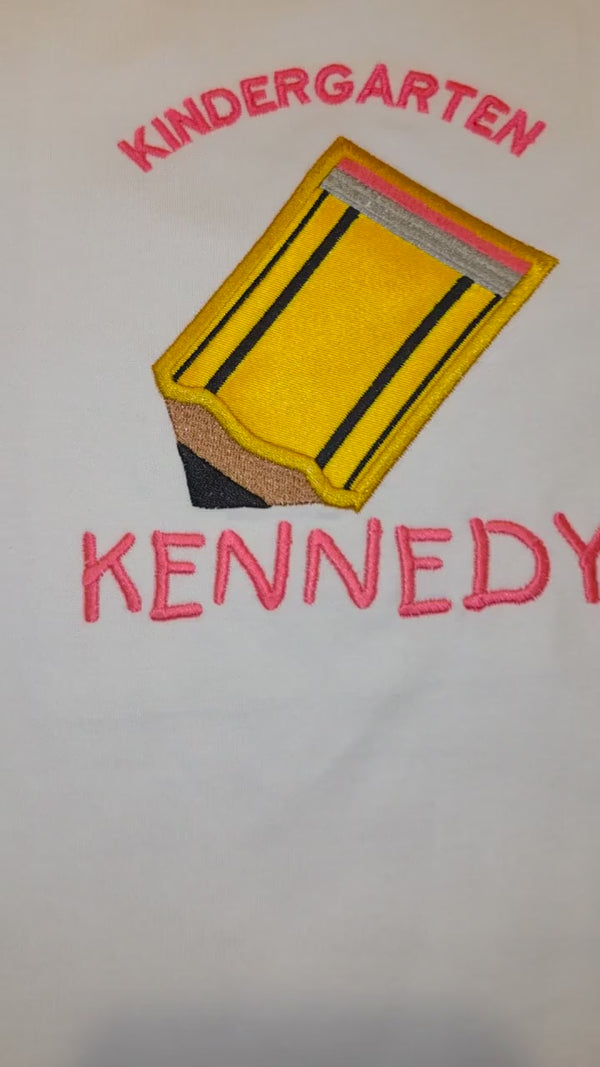 Video showing personalized white girls’ ruffle shirt with Kindergarten embroidery, pencil appliqué, and name Kennedy